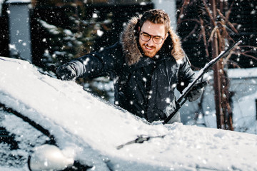 man clearing snow off car in winter