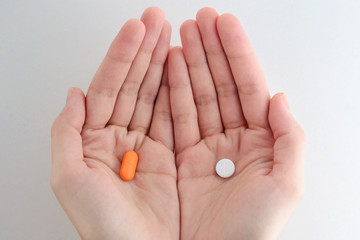 person's hands holding two different types of pills