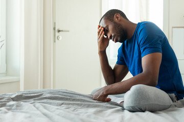 man sitting on bed holding head