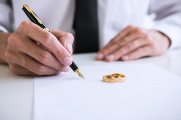 man signing divorce papers with rings